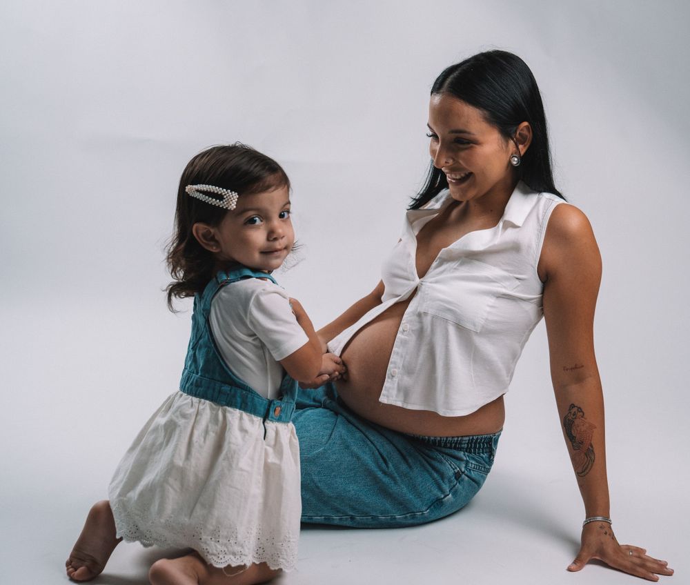 A playful mother-daughter moment against a light studio backdrop.
