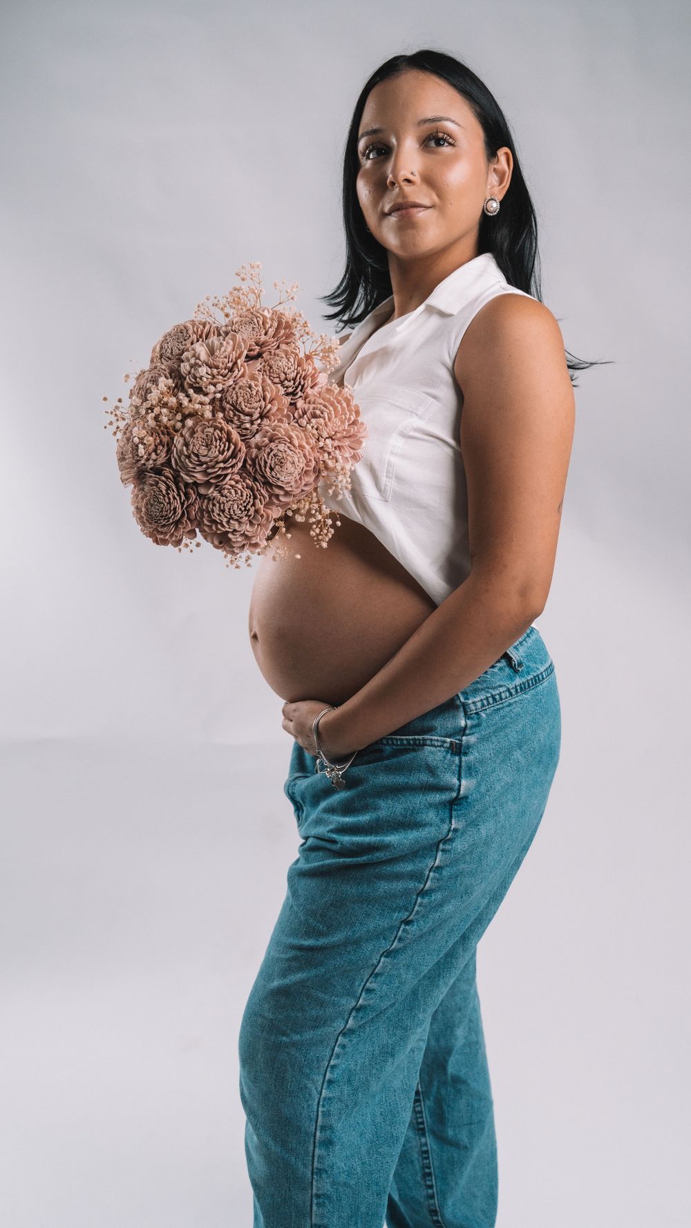 Maternity portrait with person holding blush-colored dried flower bouquet against light background.