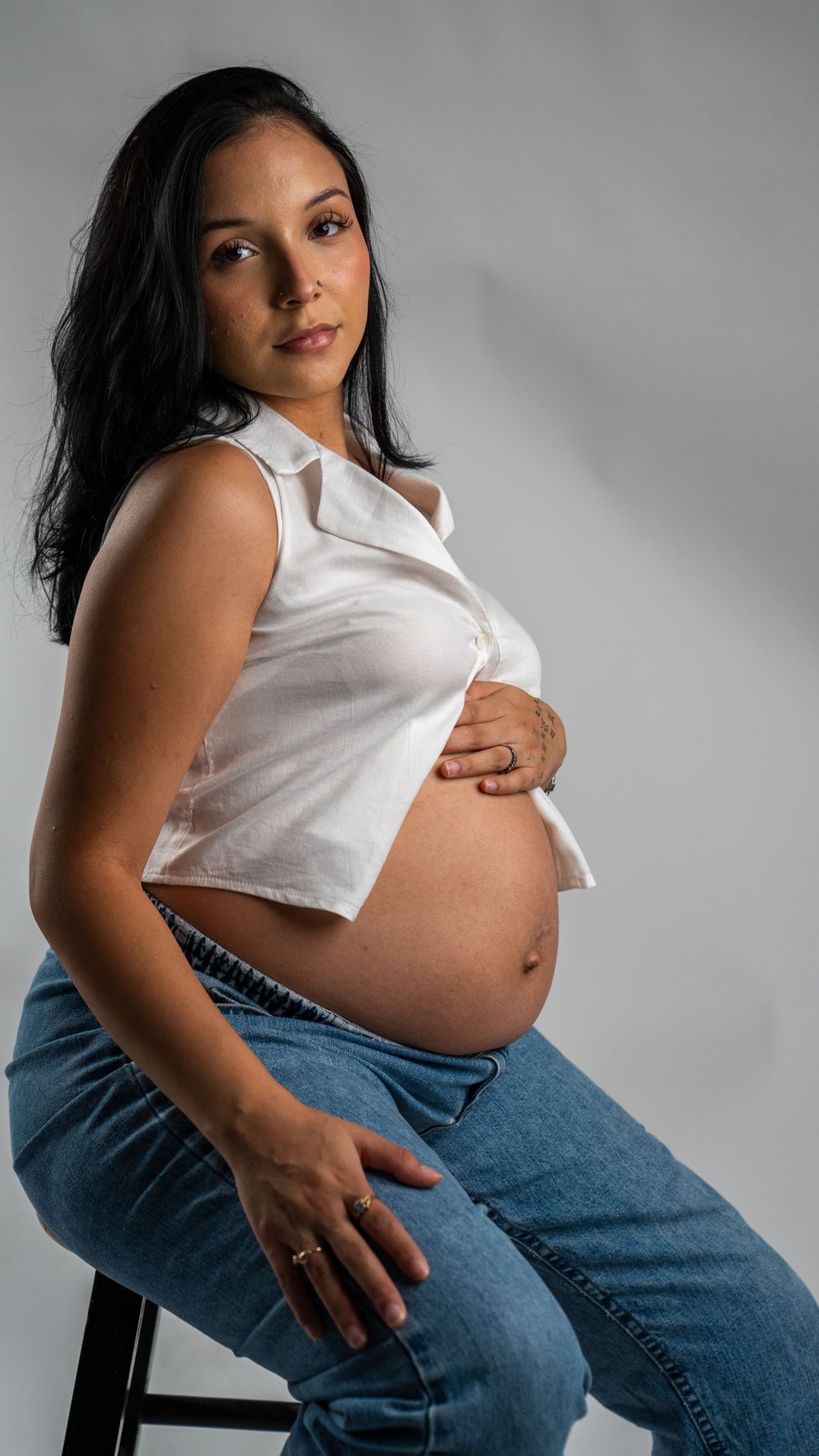 Intimate maternity portrait showing baby bump in white button-down top and blue jeans.