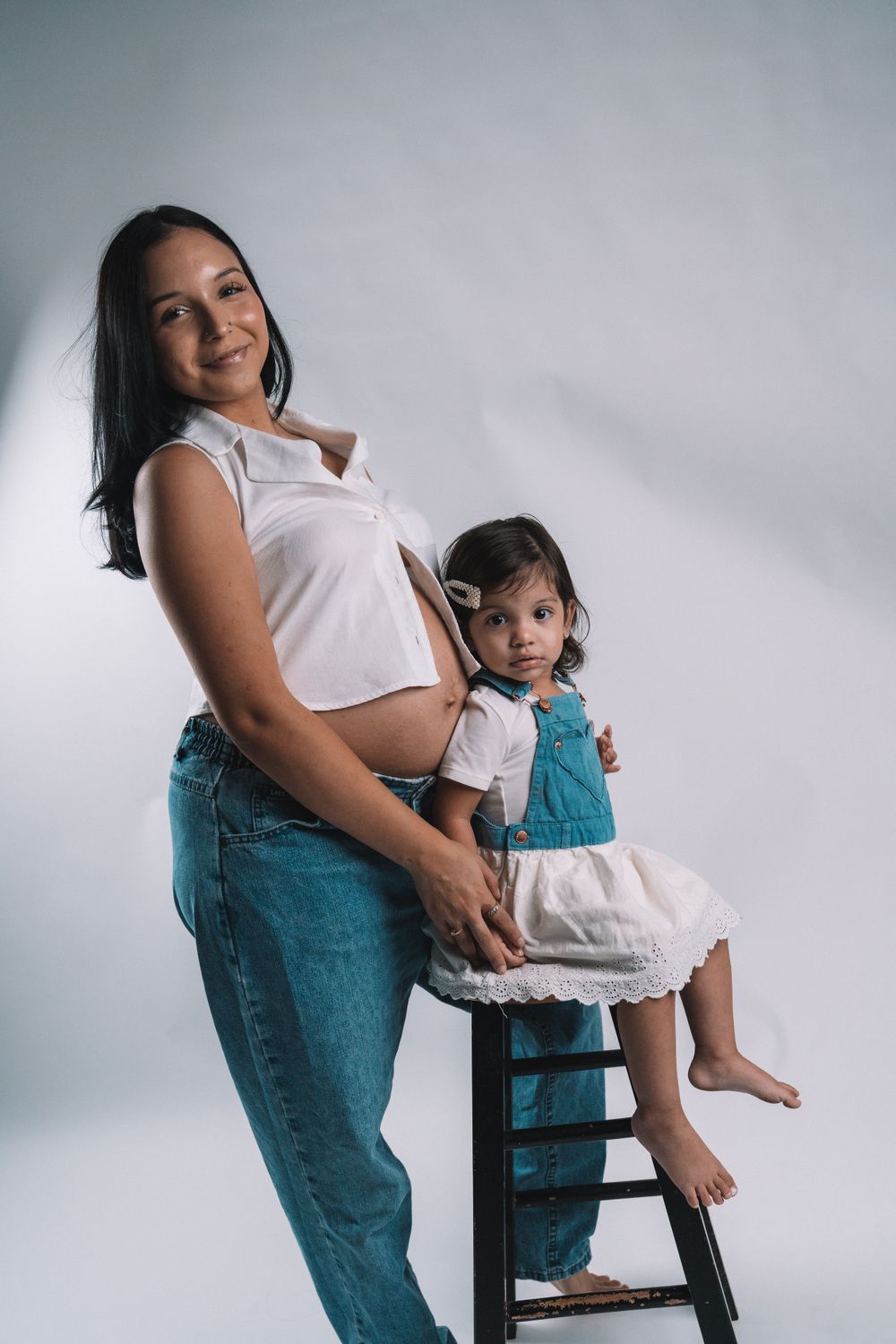 Mother and child portrait on stool against white background in matching white outfits.