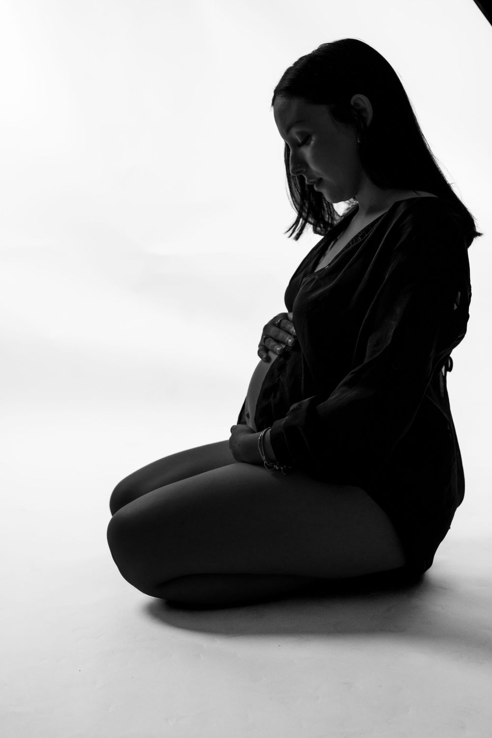 Artistic black and white silhouette of pregnant person sitting in contemplative pose.