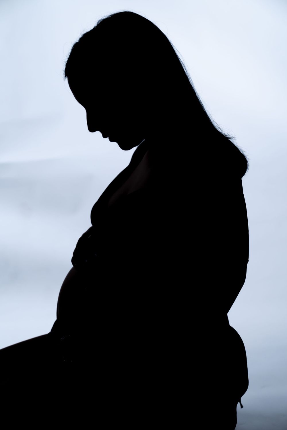 Dramatic side profile silhouette of expectant mother against light background.