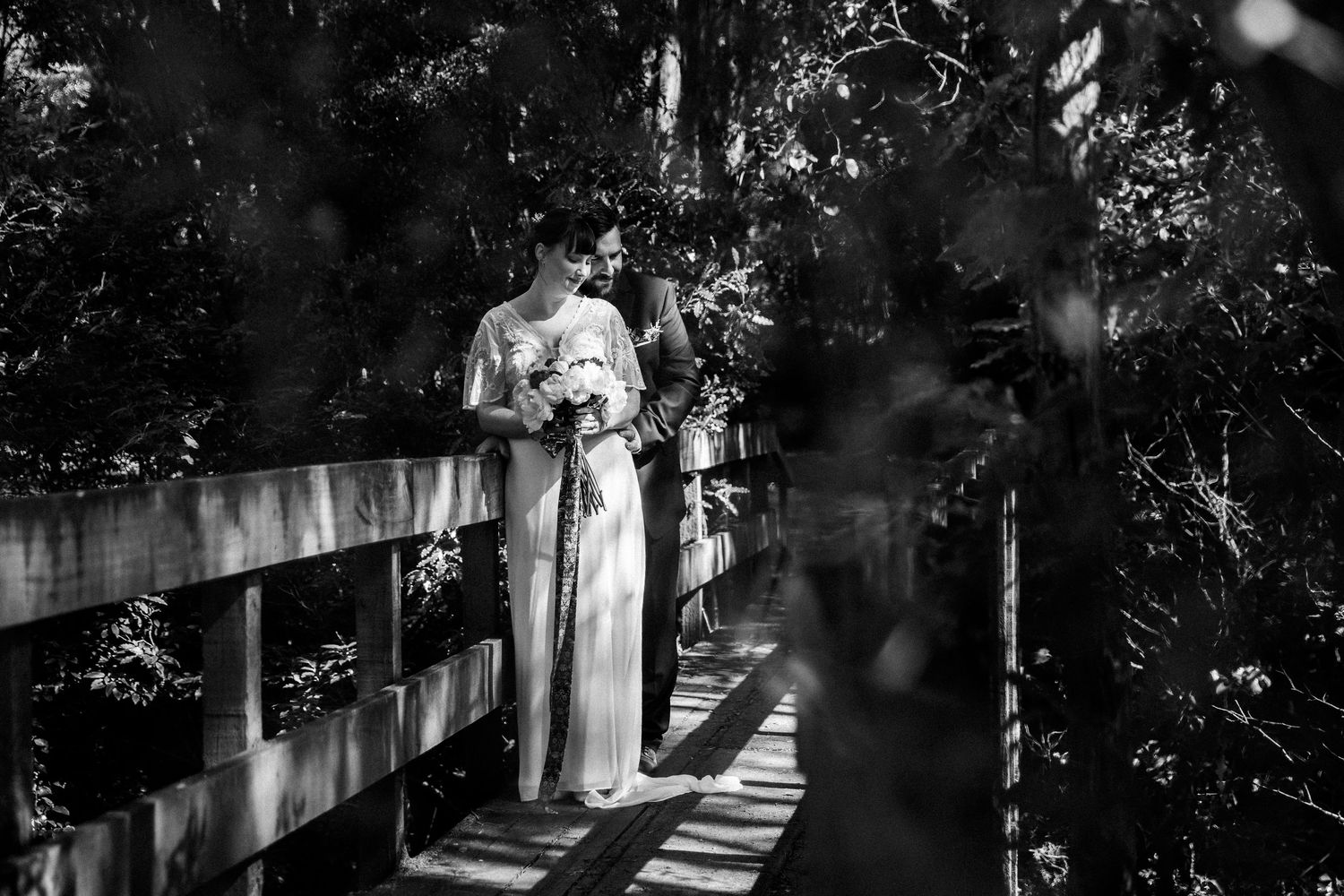 Black and white photo of wedding couple on wooden bridge with dramatic shadows.