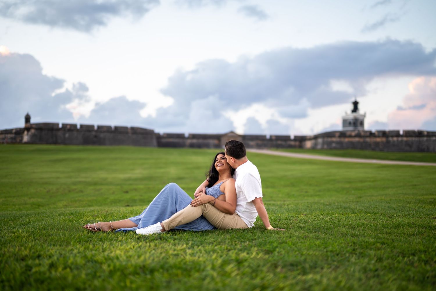 People relaxing on lush green grass at sunset near historic fortification walls.