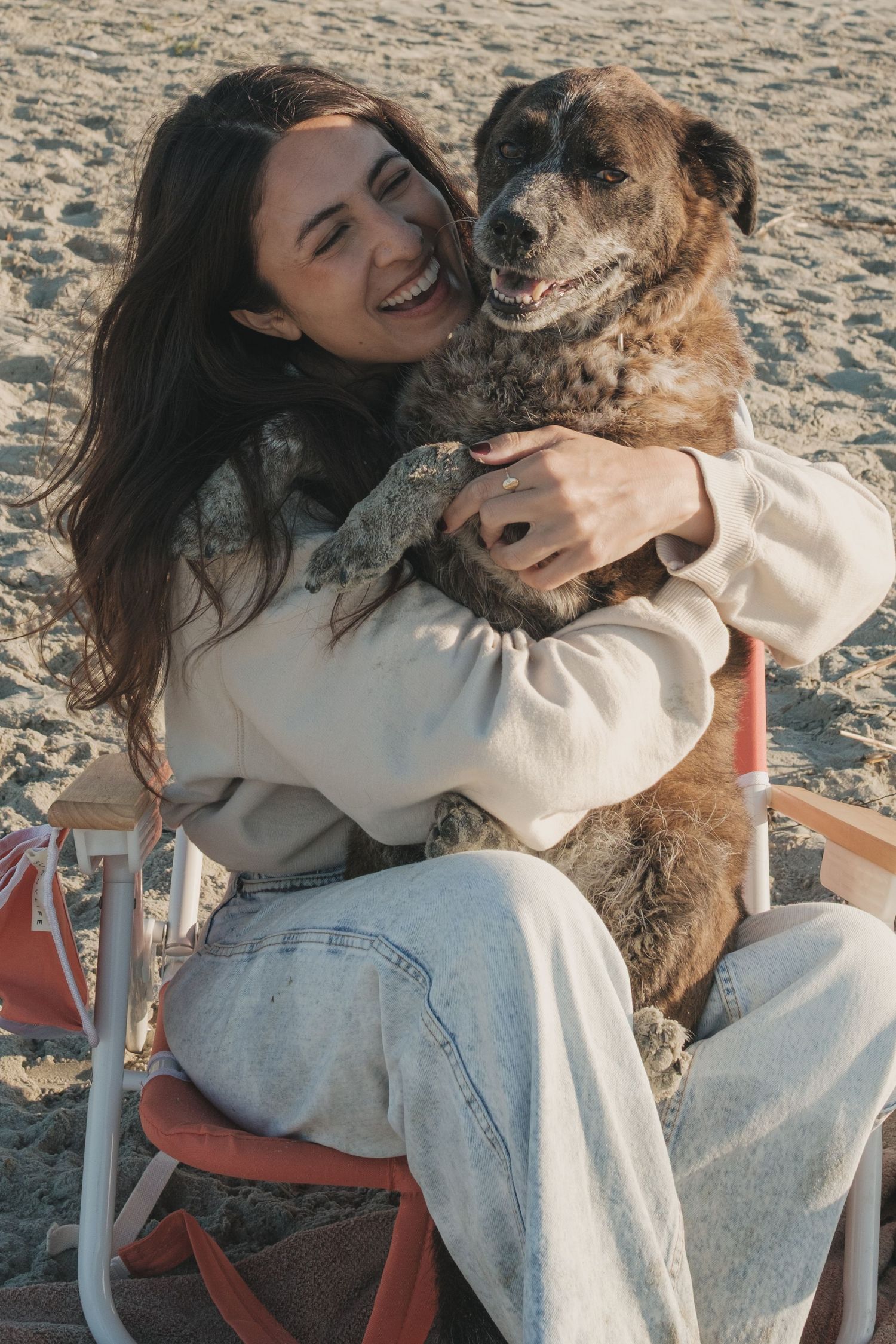 Woman sitting in a chair at the beach, holding her dog in her lap as they relax together by the ocean