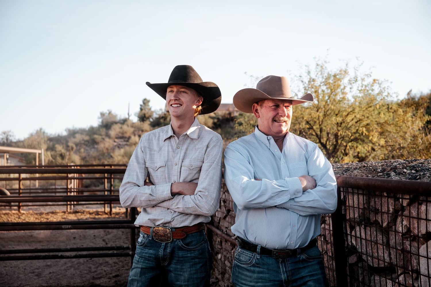 Two cowboys in western attire standing against a scenic desert background.
