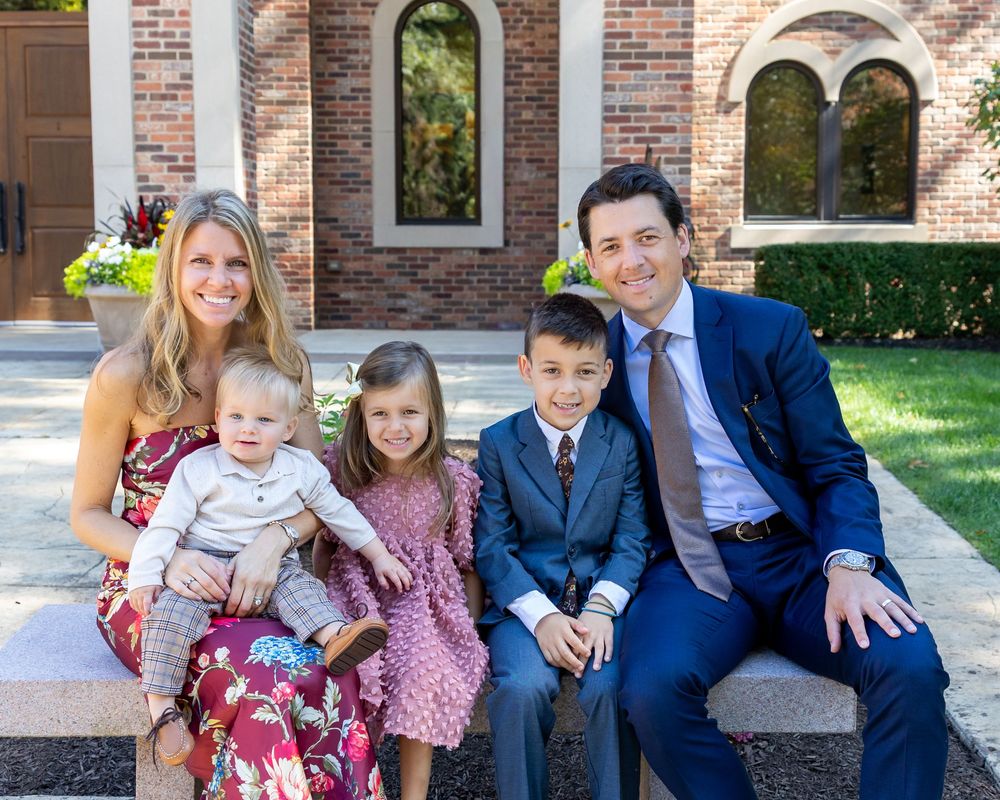 A family sits together on stone steps outside St. Demetrios Church in Weston, MA in coordinated red white and blue outfits.