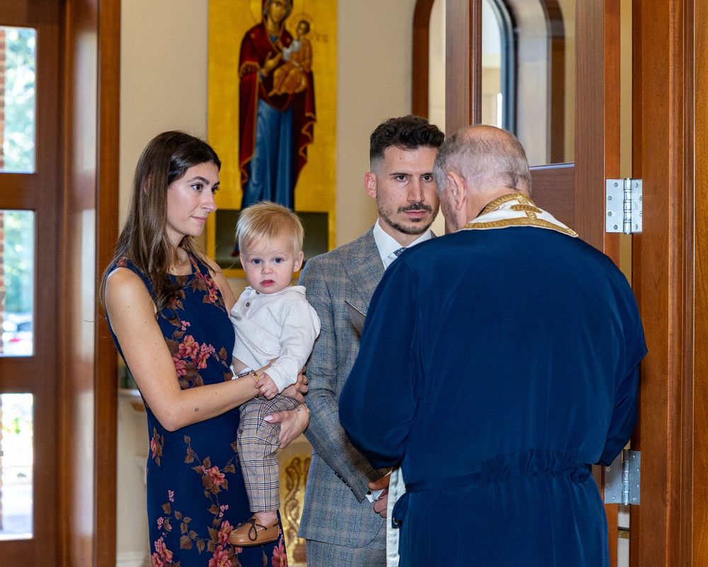 The Godparent and baby at the start of a baptism ceremony with the Priest at the head of the aisle at St. Demetrios Church in Weston, MA.