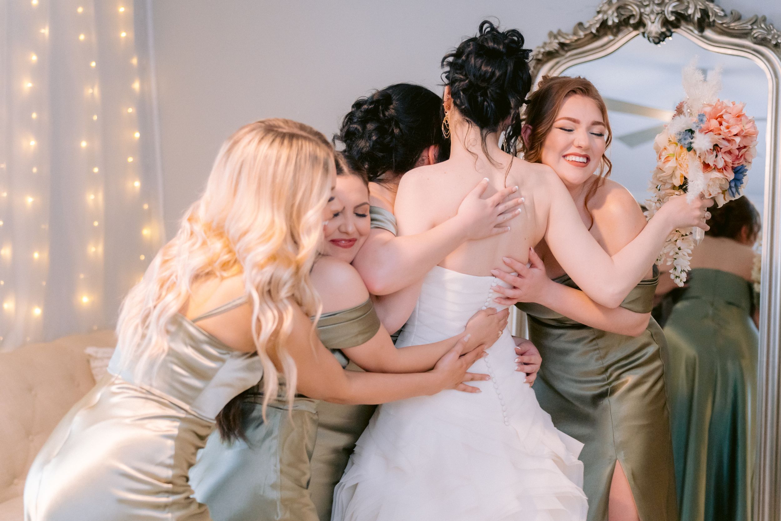 Bridesmaids in silk dresses embrace during an emotional wedding moment.
