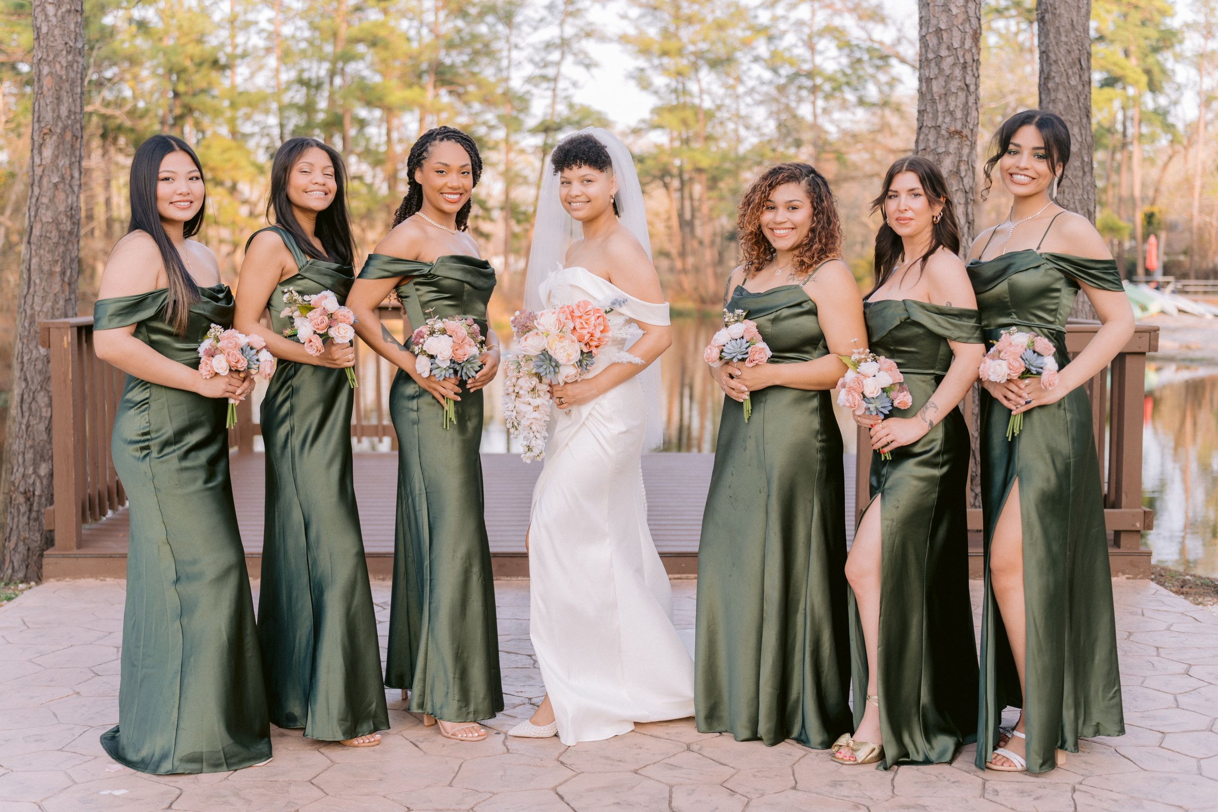 Wedding party photo with bridesmaids in emerald green dresses posing outdoors.