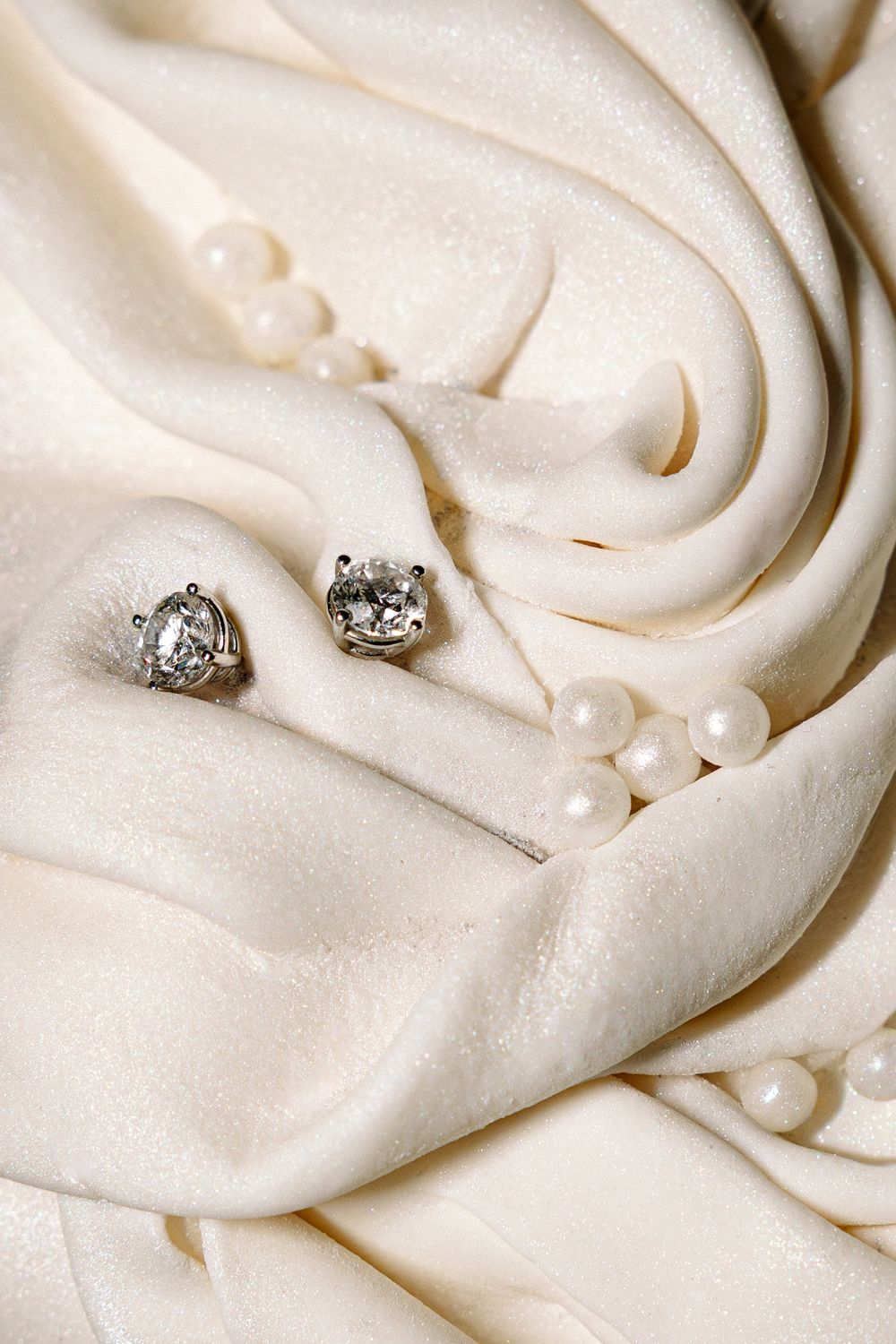 Smooth white meringue frosting swirls with delicate pearl decorations and diamond ring accents create an elegant wedding cake texture.
