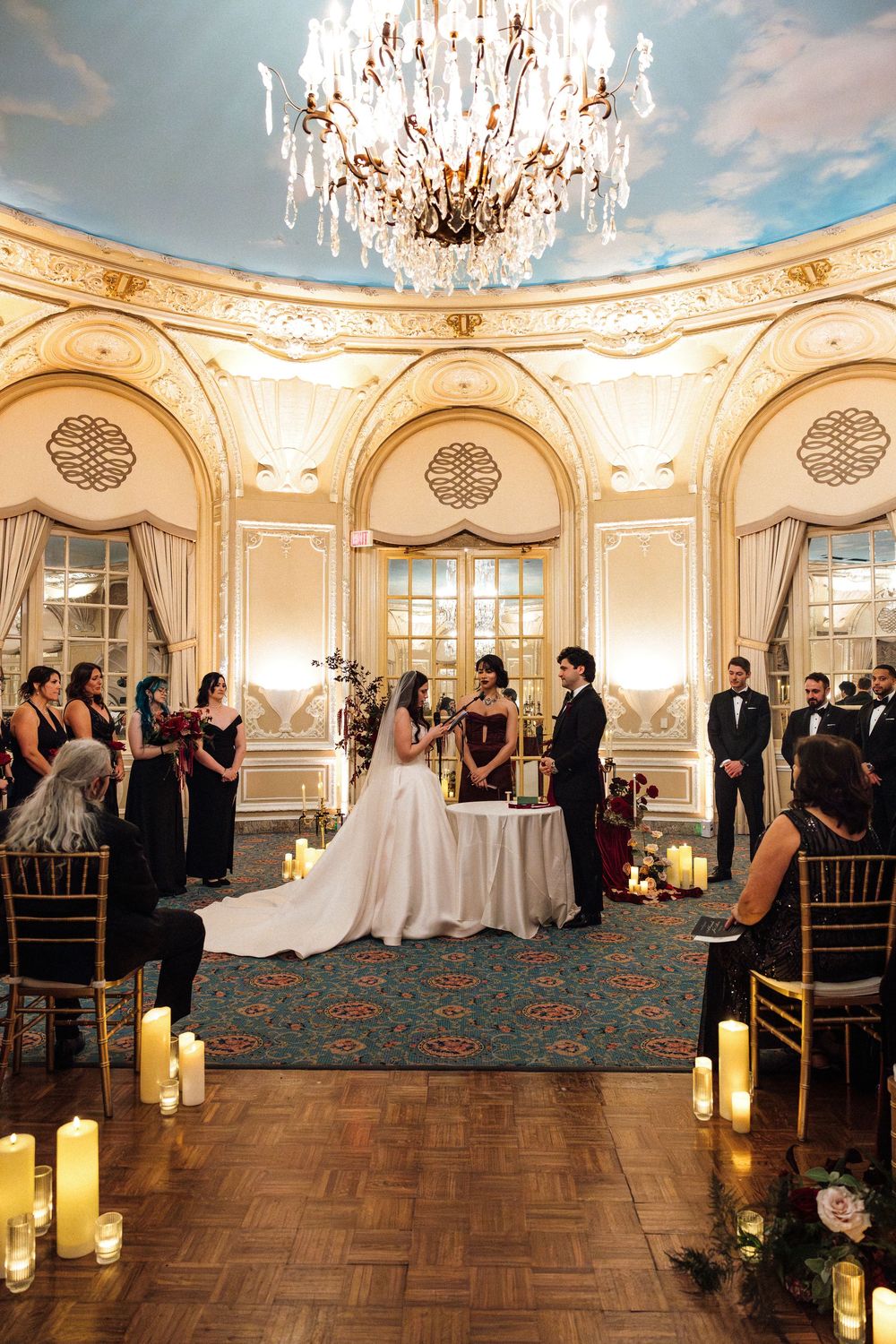 Elegant wedding ceremony panorama in ornate ballroom with crystal chandeliers, candles and parquet flooring.