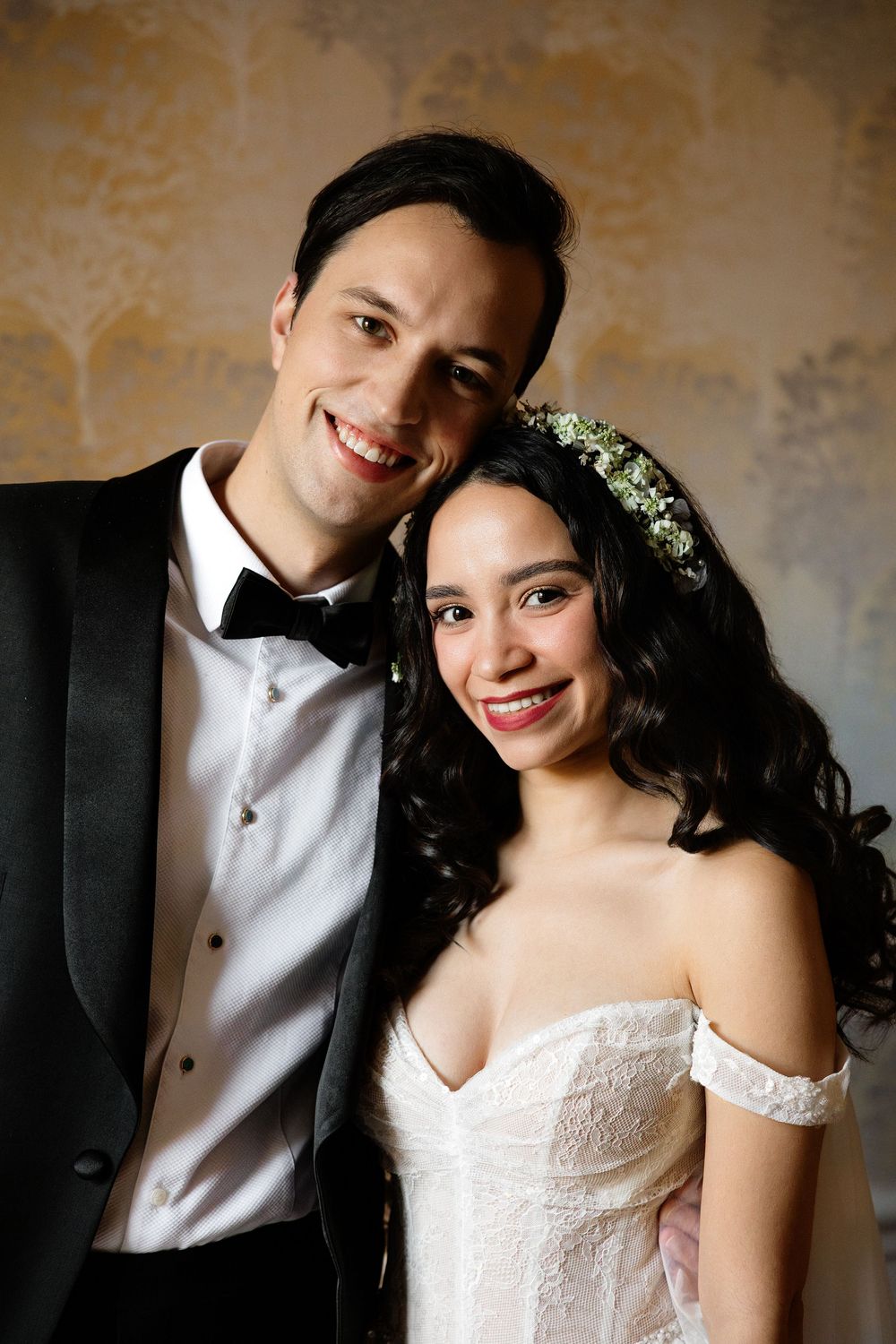 A romantic wedding portrait featuring a couple in formal attire with the bride wearing a floral crown and off-shoulder gown.