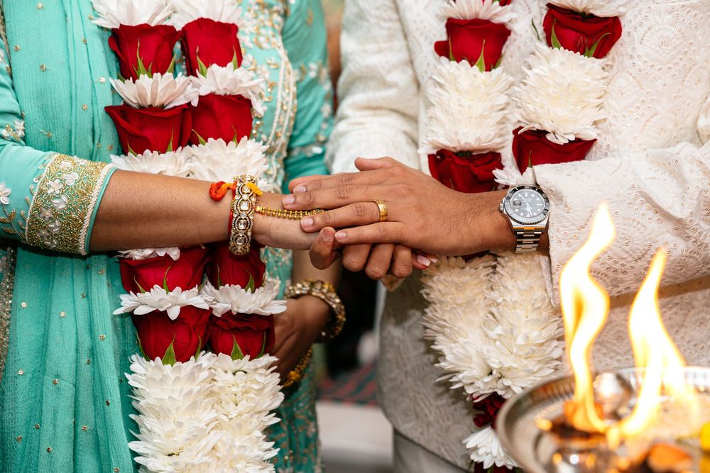 A wedding bouquet of red roses and white flowers is held against a turquoise bridesmaid dress.