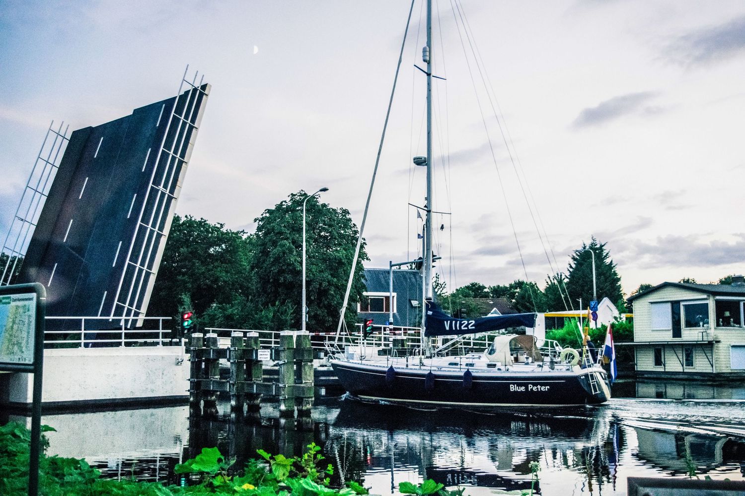 Sailboat moored next to a drawbridge in a canal under cloudy skies.