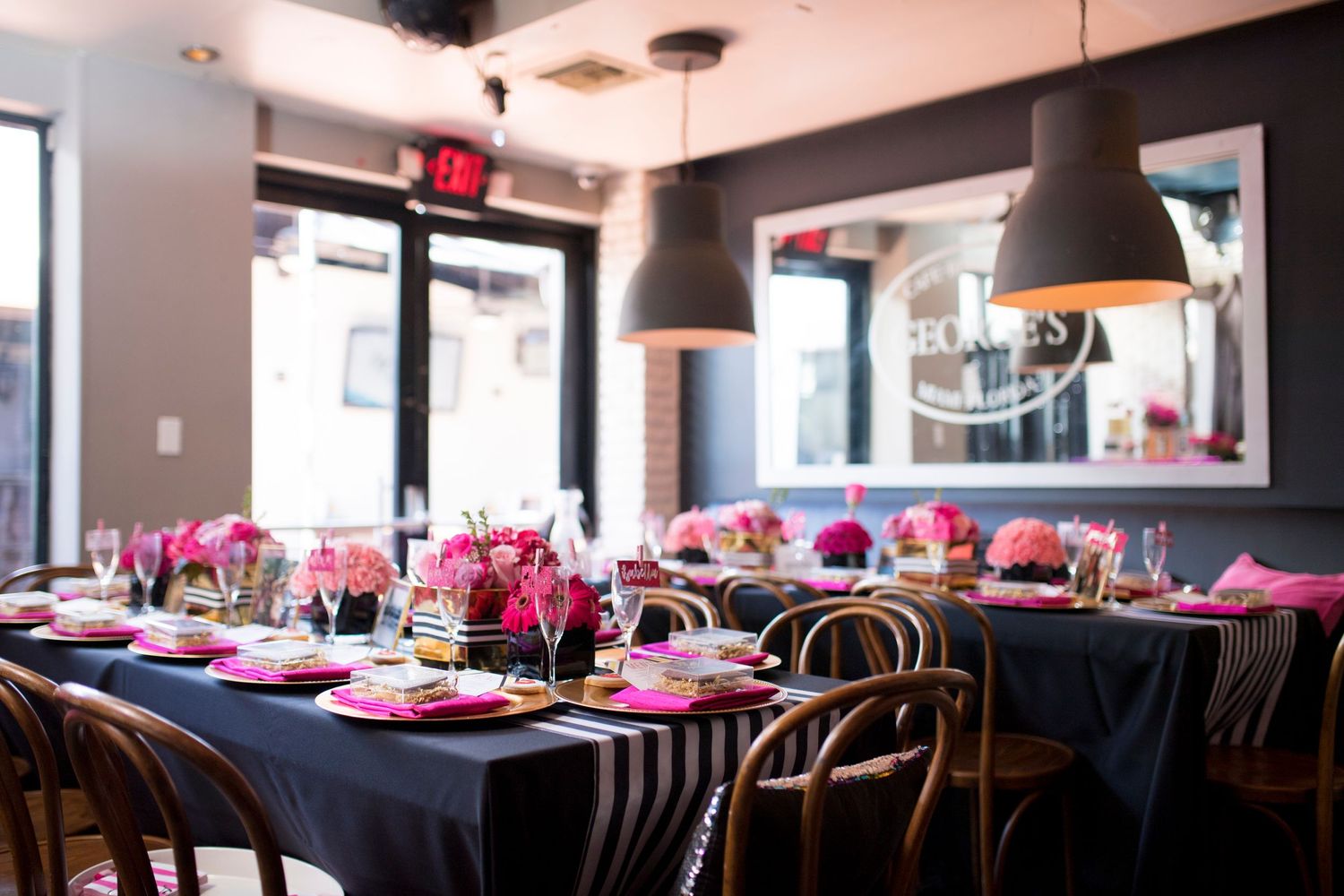 Modern restaurant interior with pink floral arrangements and black table settings.