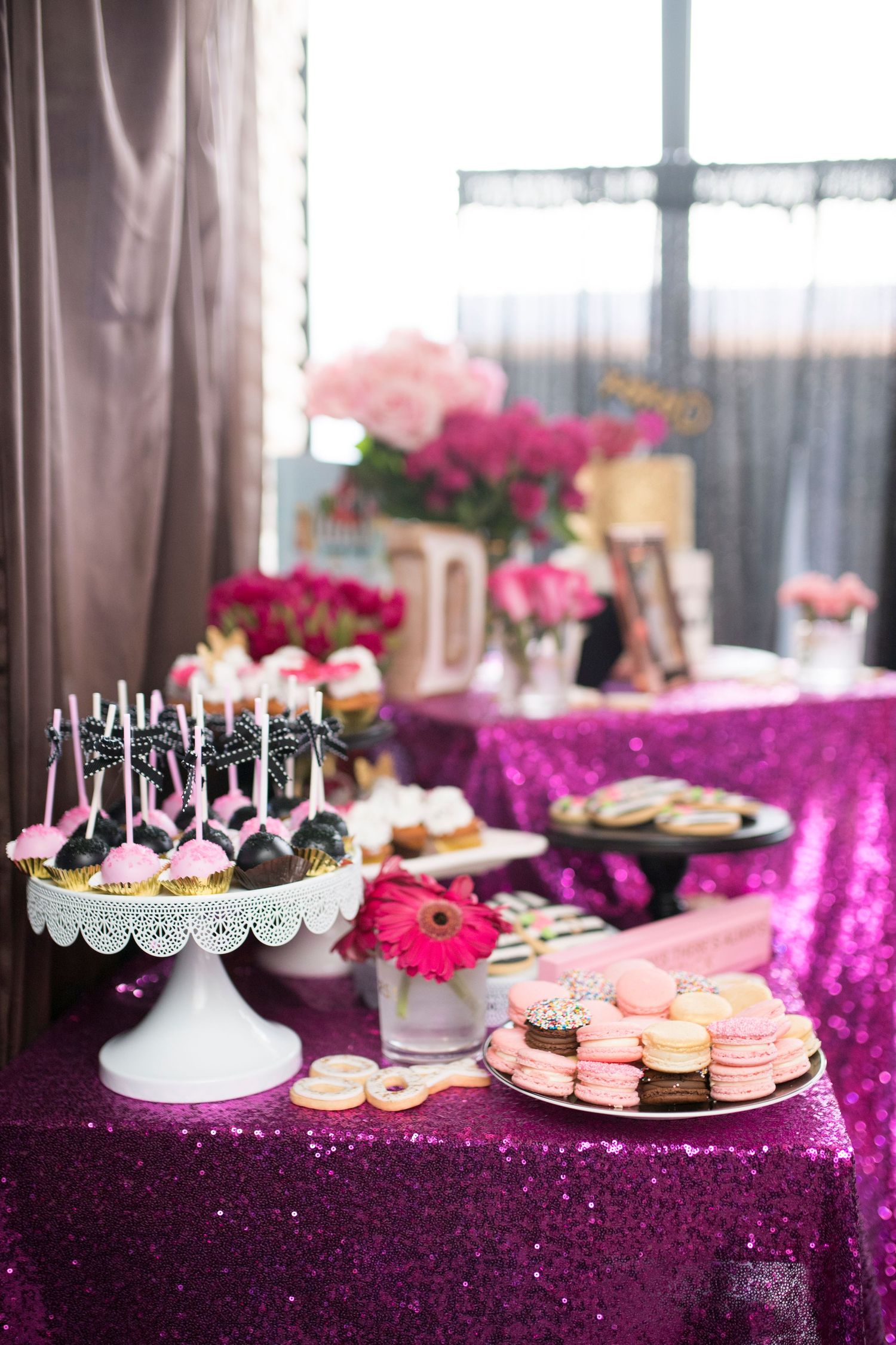 Elegant dessert table with pink and magenta decor featuring cake pops and macarons on white stands.