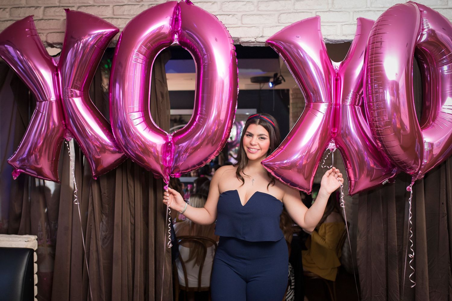 Festive party setup with large pink XOXO letter balloons against a dark backdrop.
