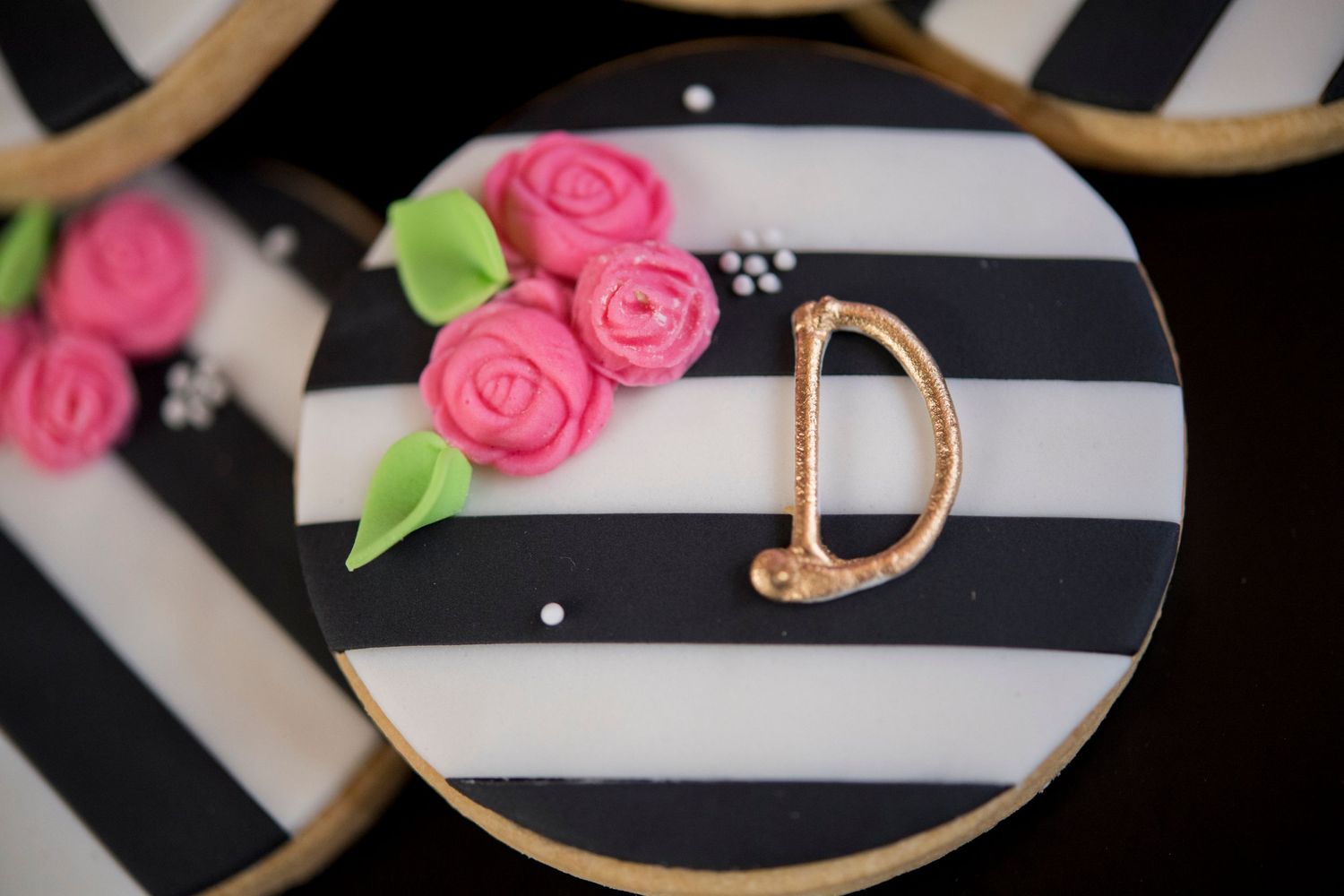 Black and white striped cookie decorated with pink fondant roses and gold monogram D.