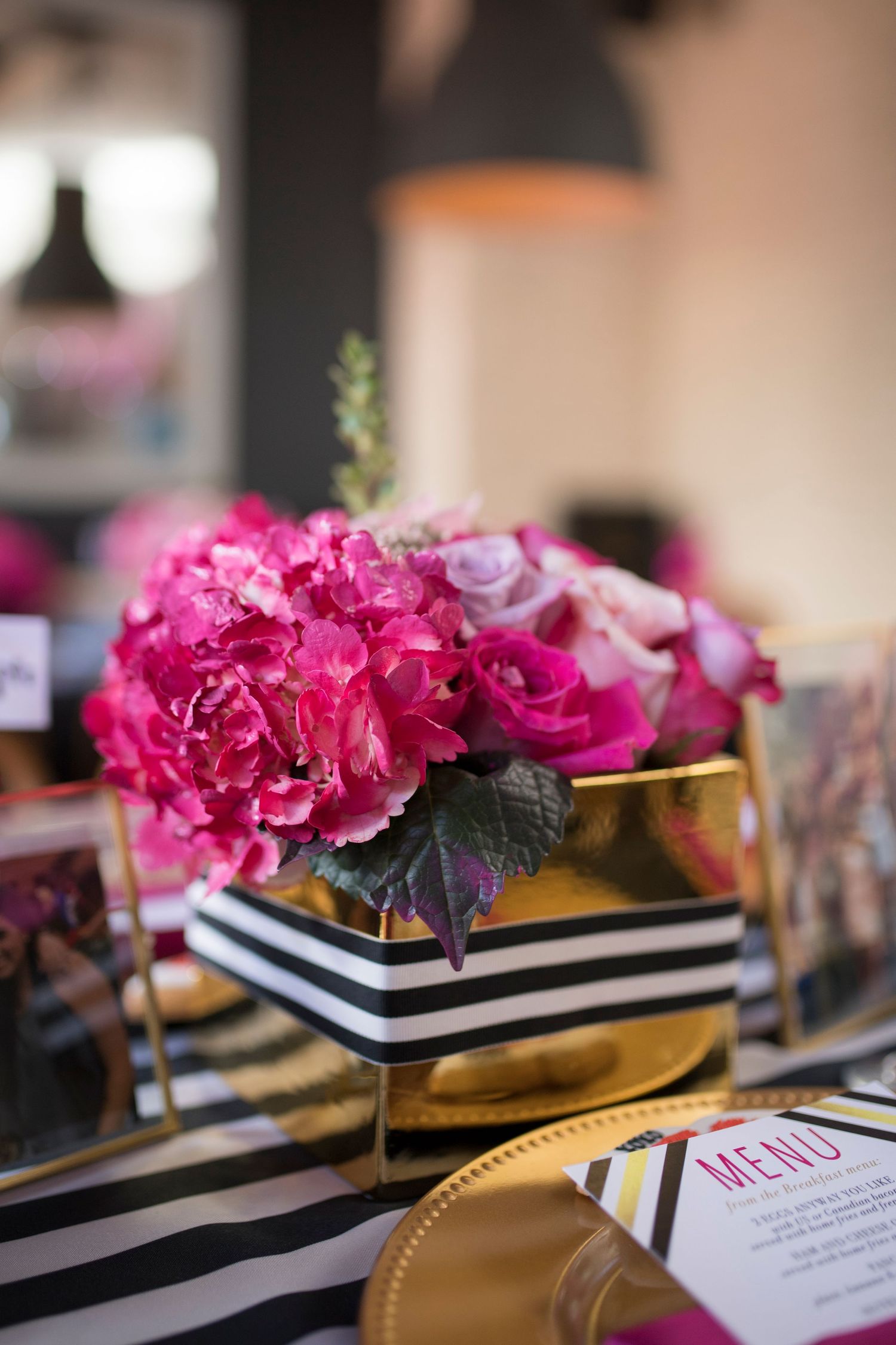 Pink roses in a gold and black striped vase create an elegant centerpiece on a striped tablecloth.