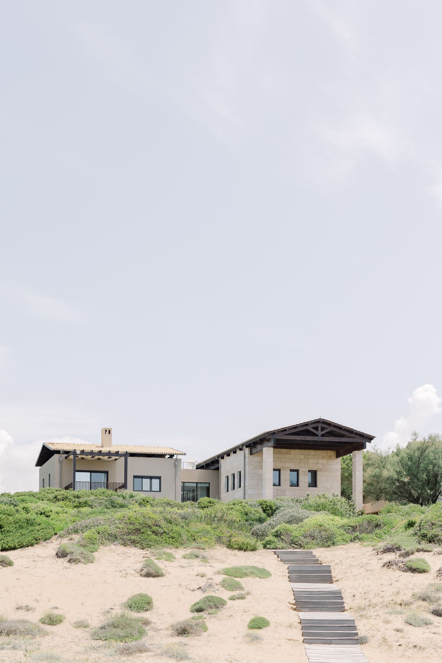 Modern beachfront homes with black stairs leading up sandy dunes against a cloudy sky.