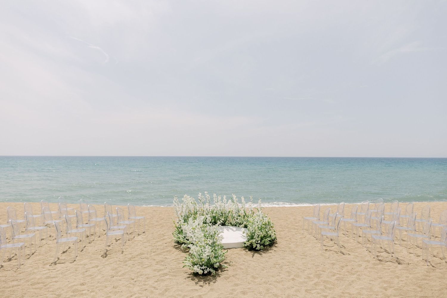 Serene beach landscape with soft blue ocean waters and sandy shore stretches to the horizon under cloudy skies.