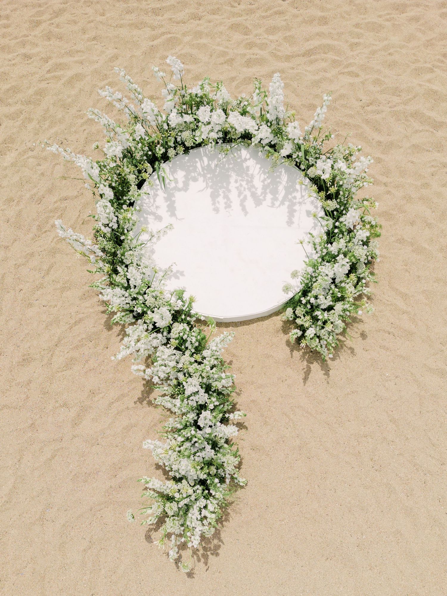 Decorative floral frame overlay with white and green foliage arranged in a circular wreath design on beige background.