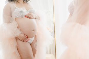 Soft focus maternity mirror portrait with delicate white lingerie and pink tulle.