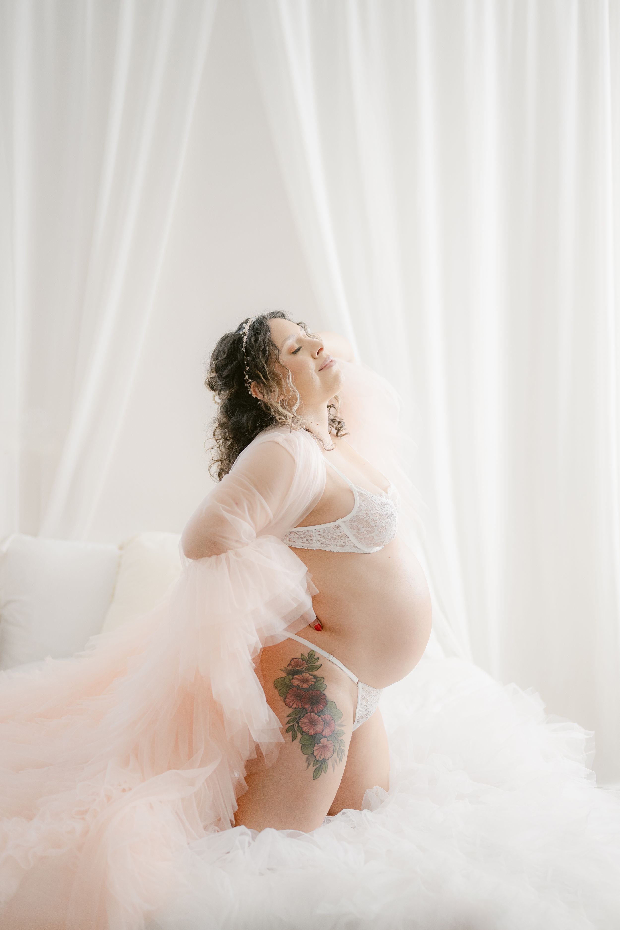 Ethereal maternity portrait with tulle and lace against white curtains.