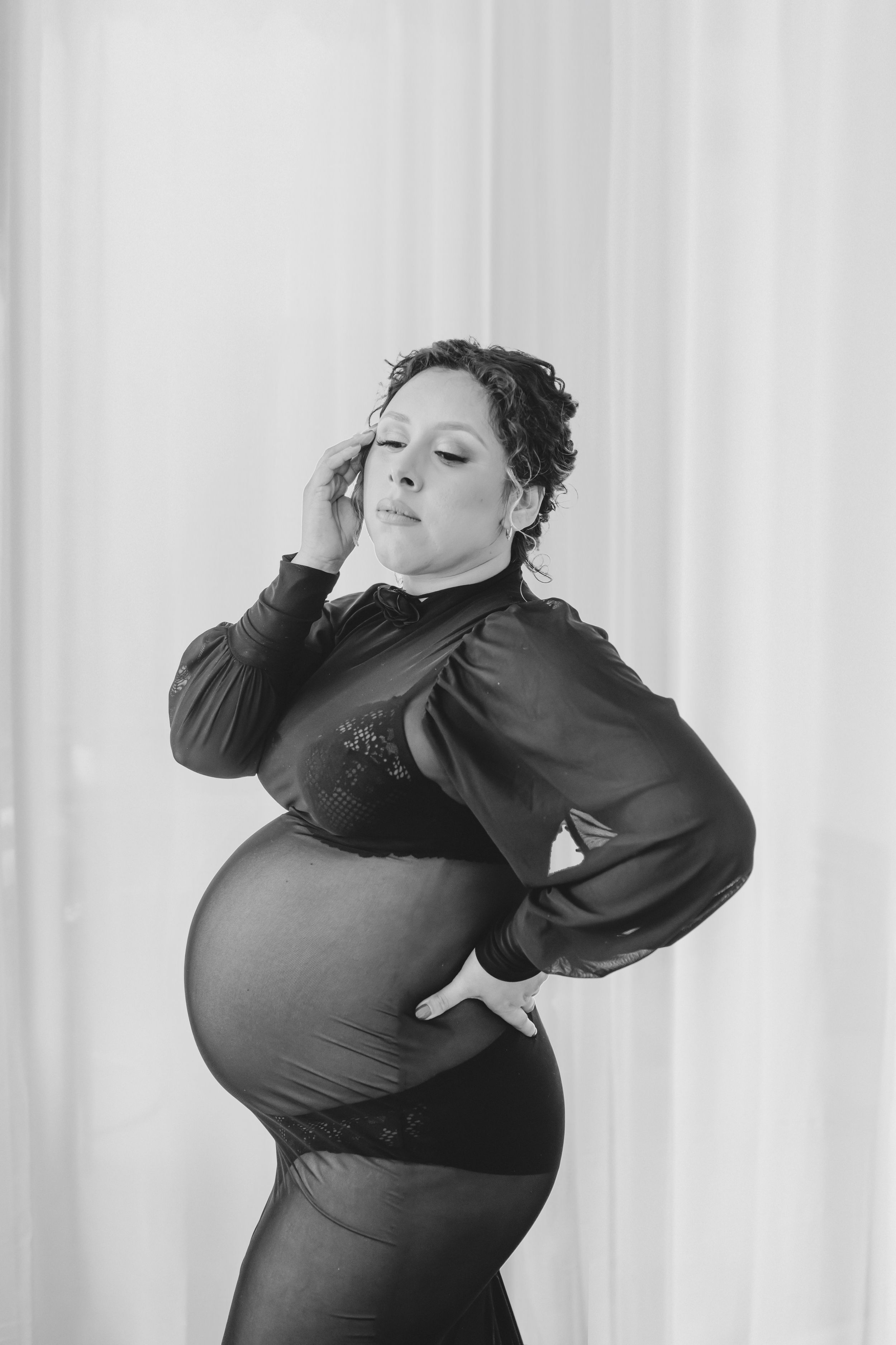Artistic black and white maternity photo showing pregnant figure in elegant dark dress against white backdrop.