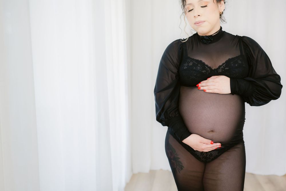 Dramatic maternity portrait in sheer black outfit highlighting pregnancy silhouette.