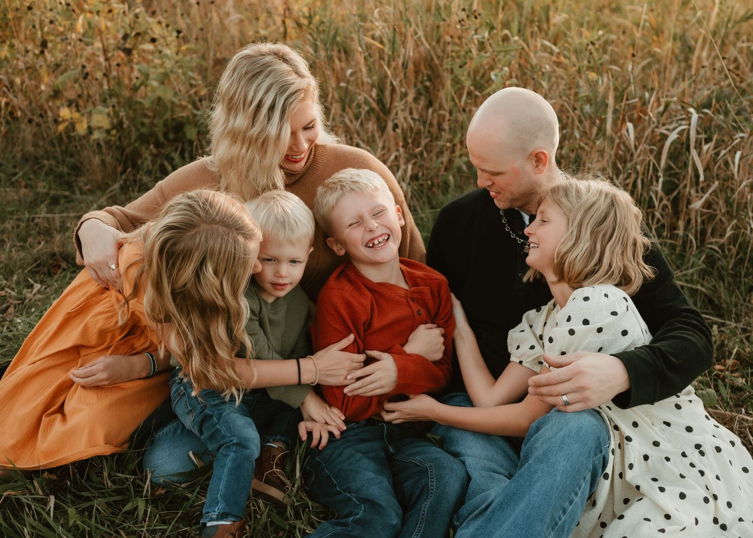 A joyful family laughing together while sitting in a golden field at sunset.