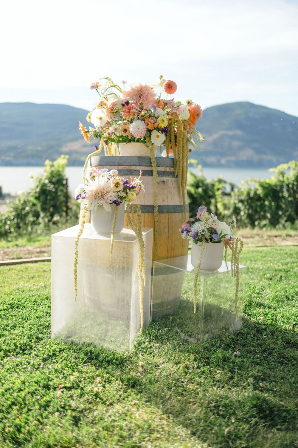 Rustic wine barrel floral arrangements set against a scenic mountain backdrop on grassy hillside.