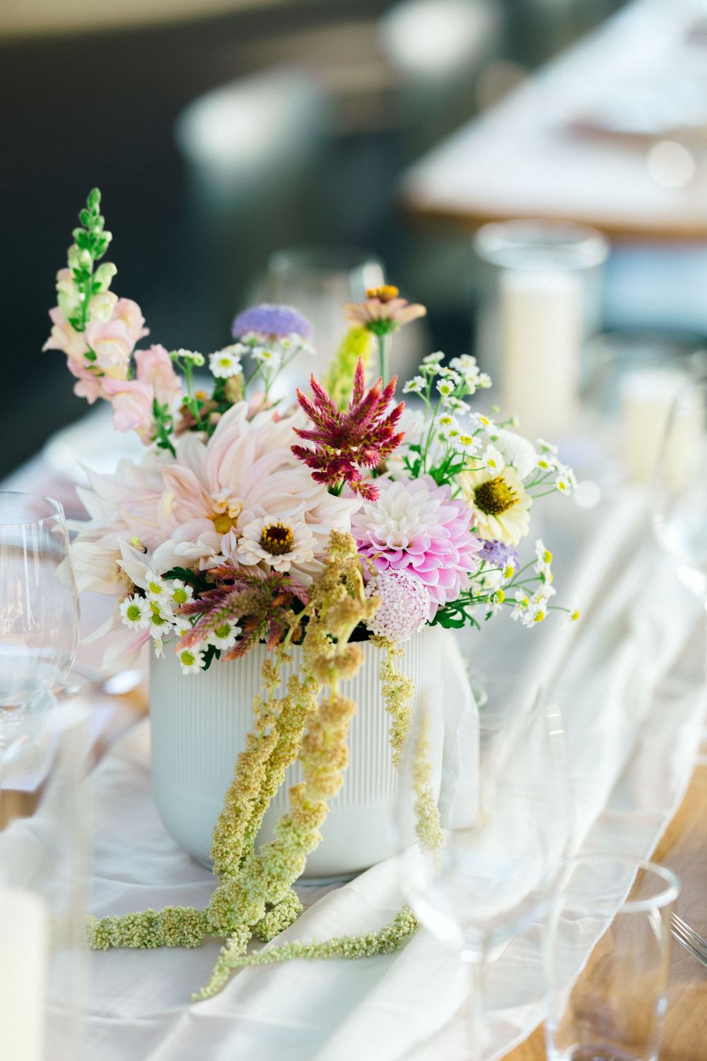 Delicate floral centerpieces with pink blooms and greenery in white vases on wedding reception table.