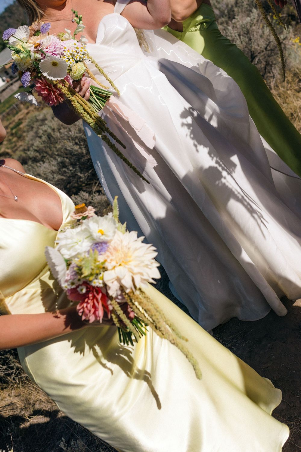 Close-up of bridal party members holding colorful wildflower bouquets against white and yellow dresses.