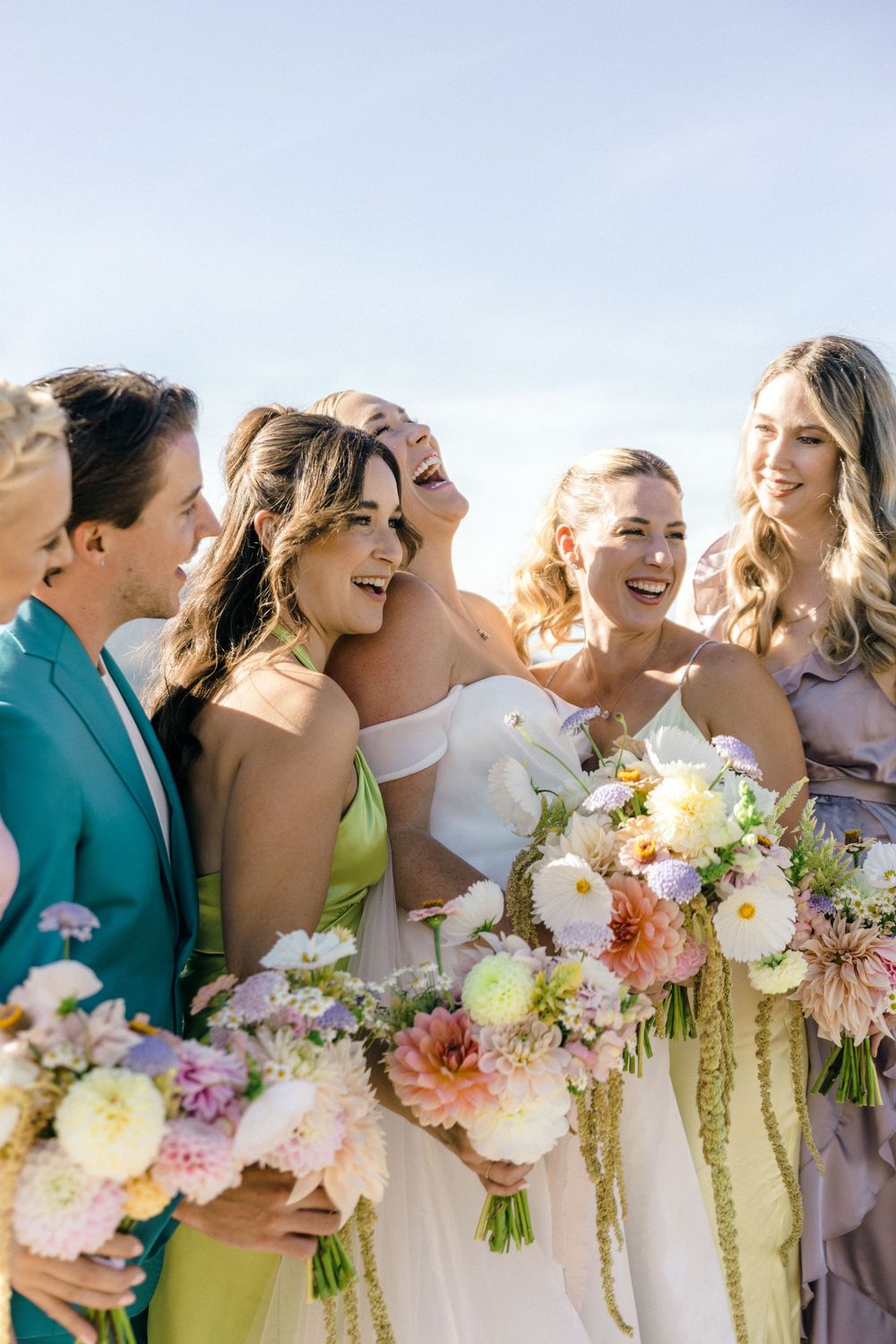 Wedding party holds colorful bouquets while laughing together outdoors.Modern Wedding in the Okanagan