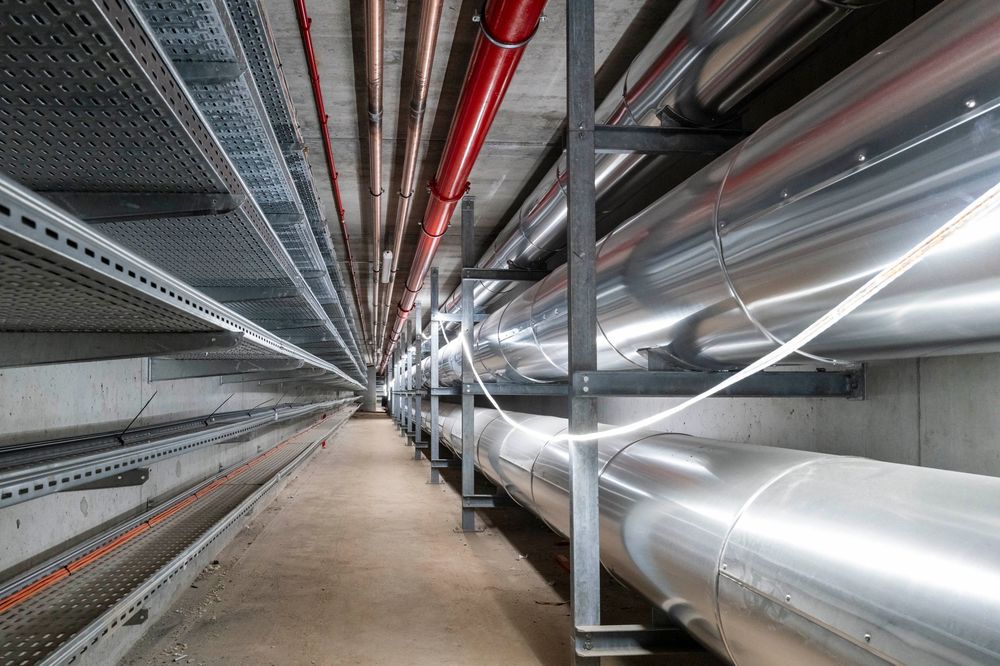 Long industrial corridor with bright fluorescent lighting and metal ductwork visible along the ceiling.