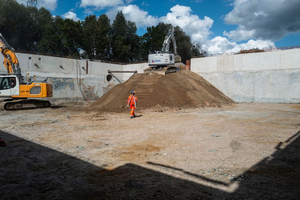 Construction site showing excavation work with machinery and dirt piles against a blue cloudy sky.