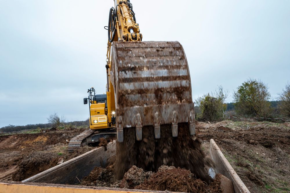 Close-up of a large excavator bucket digging into muddy soil on a construction site.