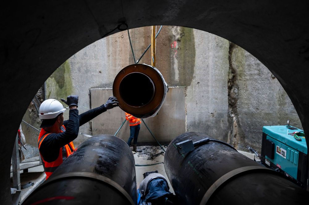 Workers install large industrial pipes inside a concrete tunnel during underground infrastructure construction.