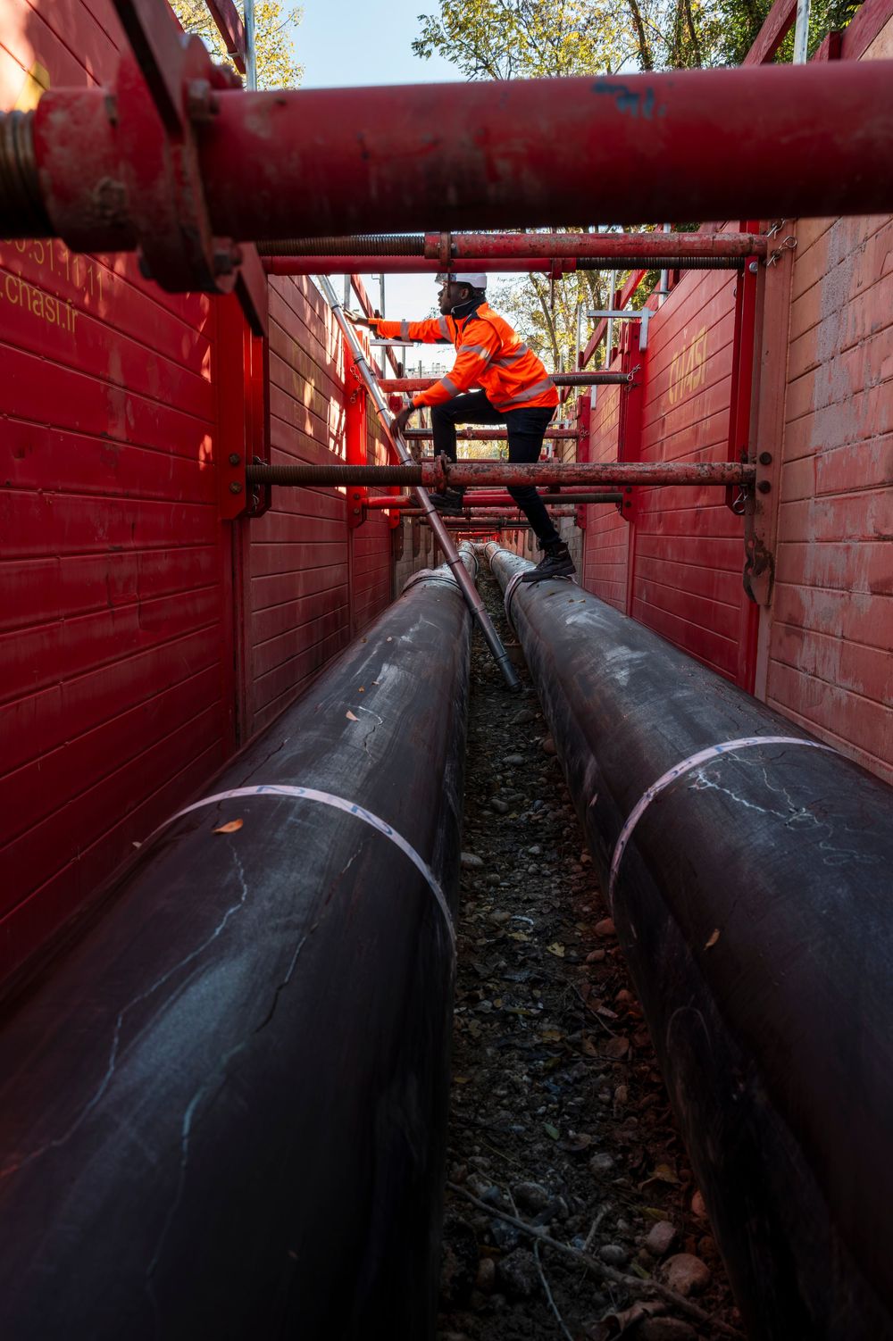 Industrial pipeline installation showing black pipes running through a red-painted tunnel structure with maintenance access.
