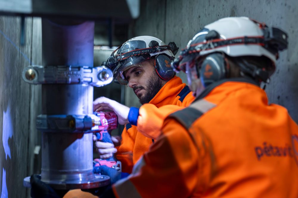Rescue workers in bright orange protective gear operate machinery in a dark industrial setting.