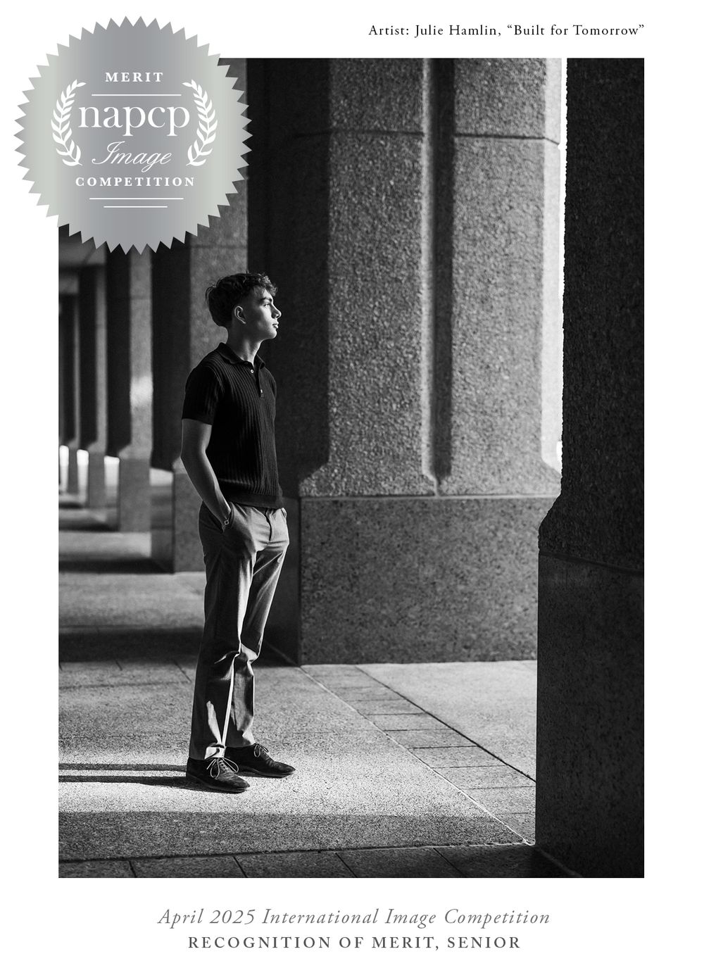 Black and white photograph of a person gazing upward in an architectural corridor with stone columns and Merit Award banner.