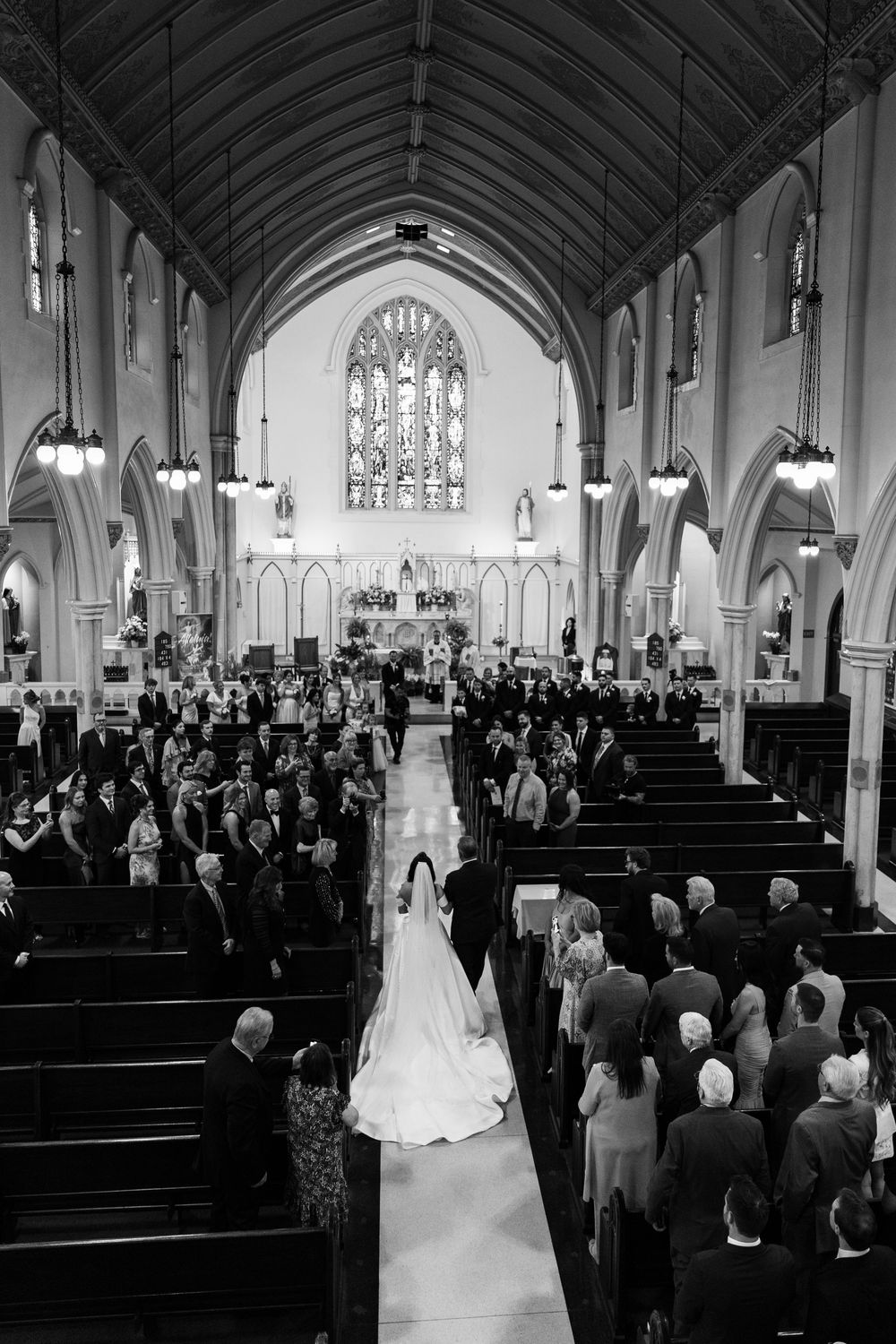 Wedding ceremony in a grand cathedral with arched ceilings and wooden pews filled with attendees.