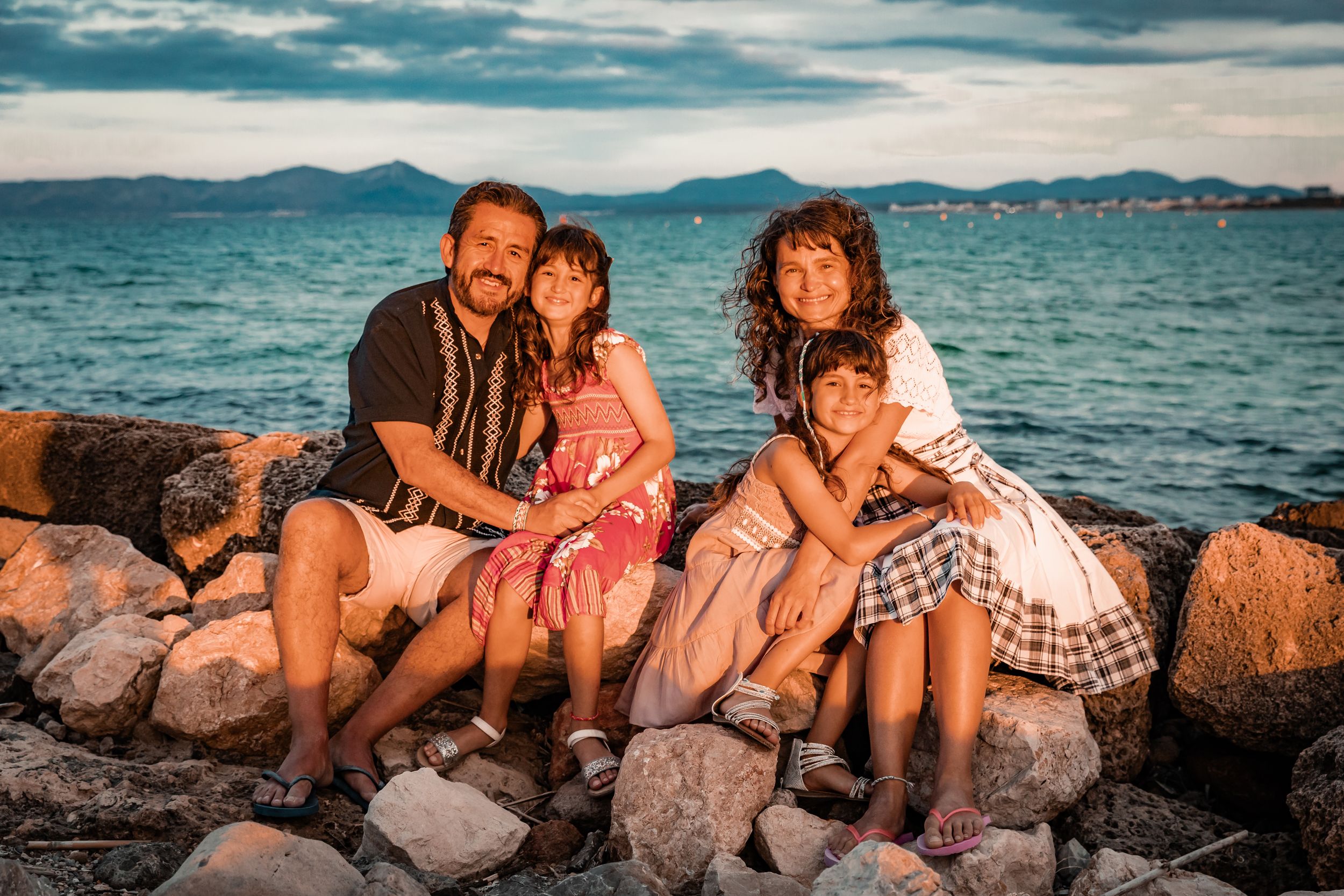 A family smiling together while sitting on coastal rocks during a lifestyle vacation photo session in Mallorca.