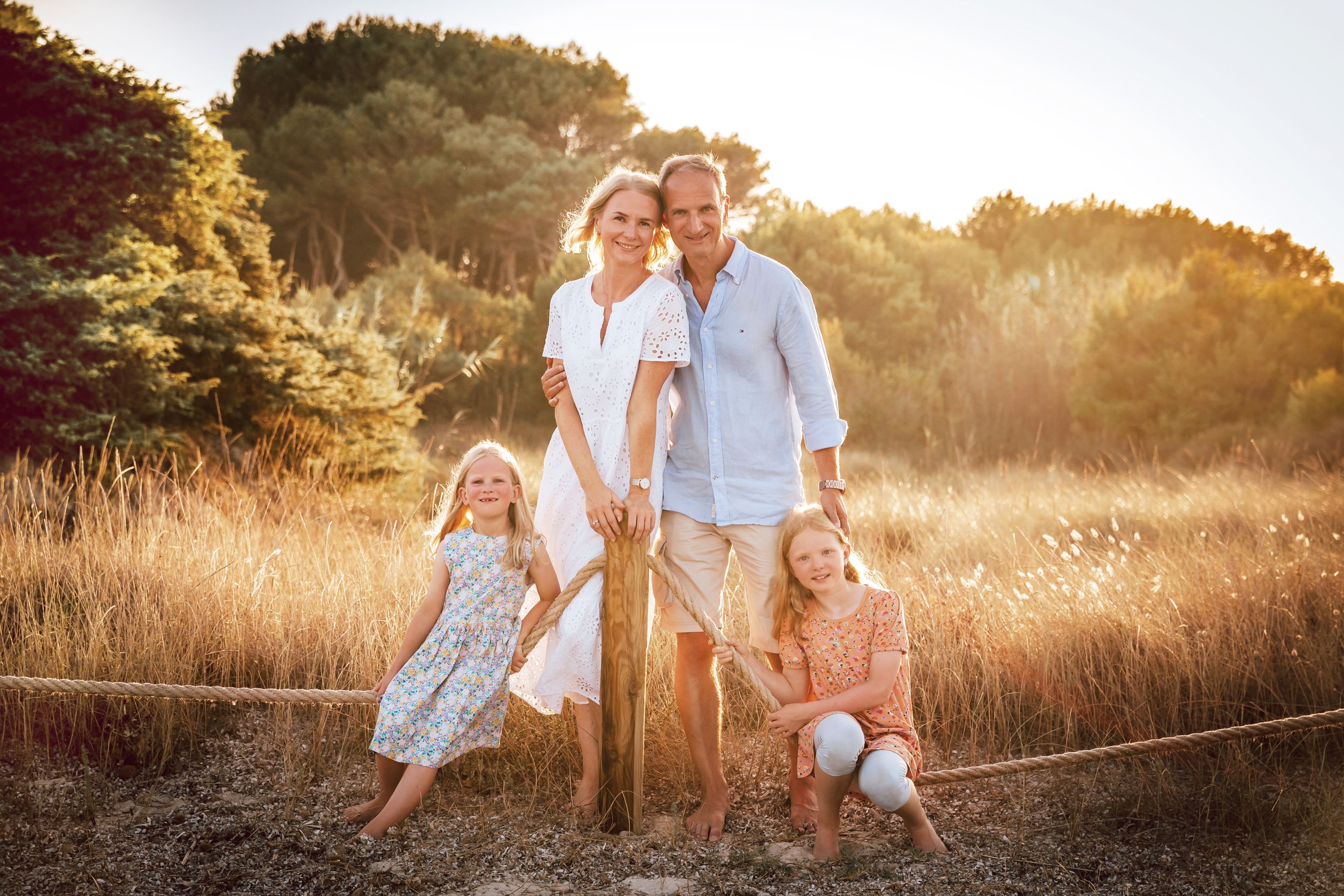 A family posing together in a sun-drenched golden field during a lifestyle vacation photo session in Mallorca.