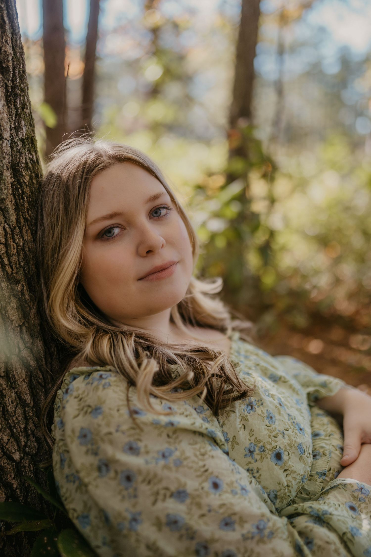 A girl with blonde hair leaning against a tree