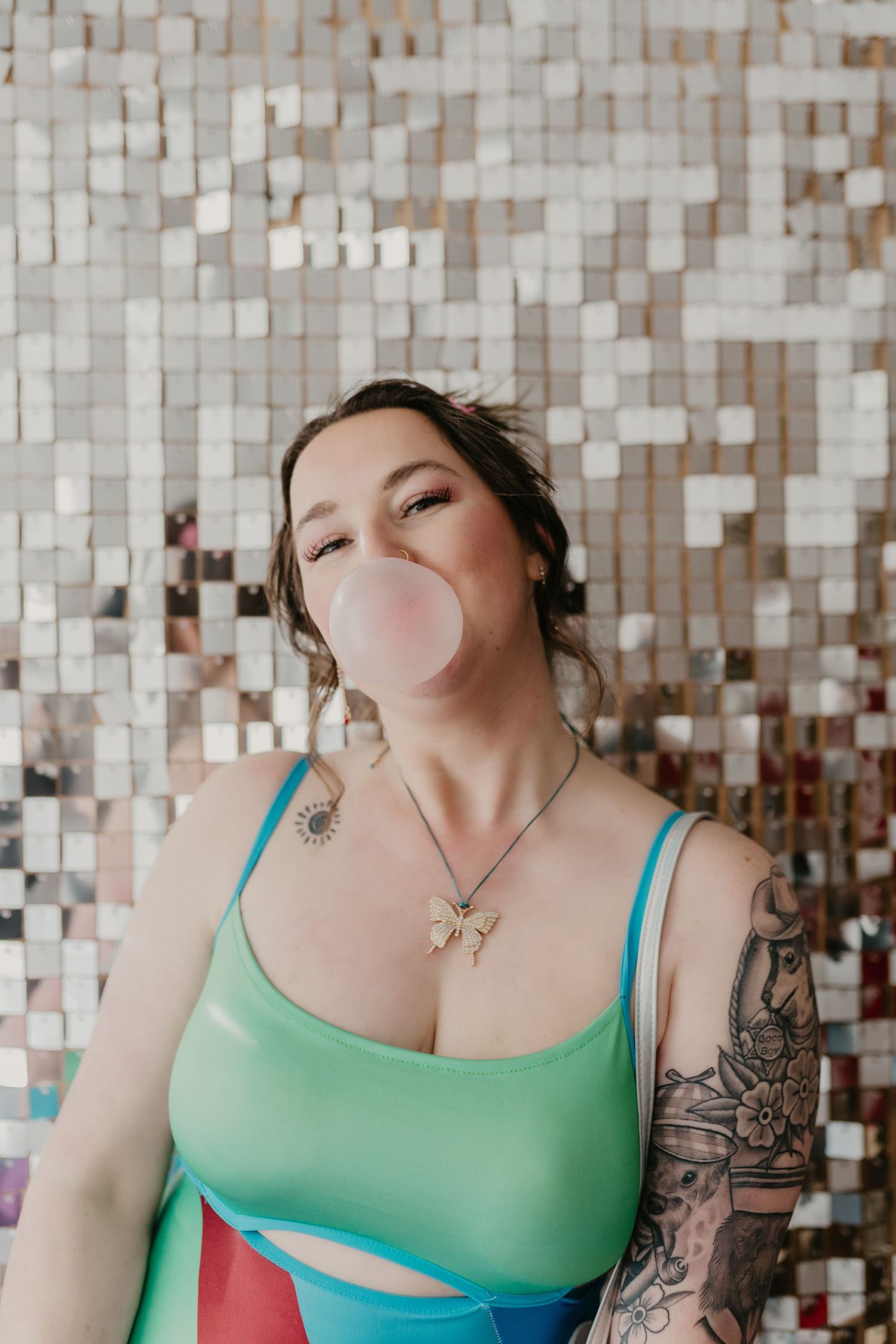 girl blowing a bubble with bubble gum in front of a disco ball wall