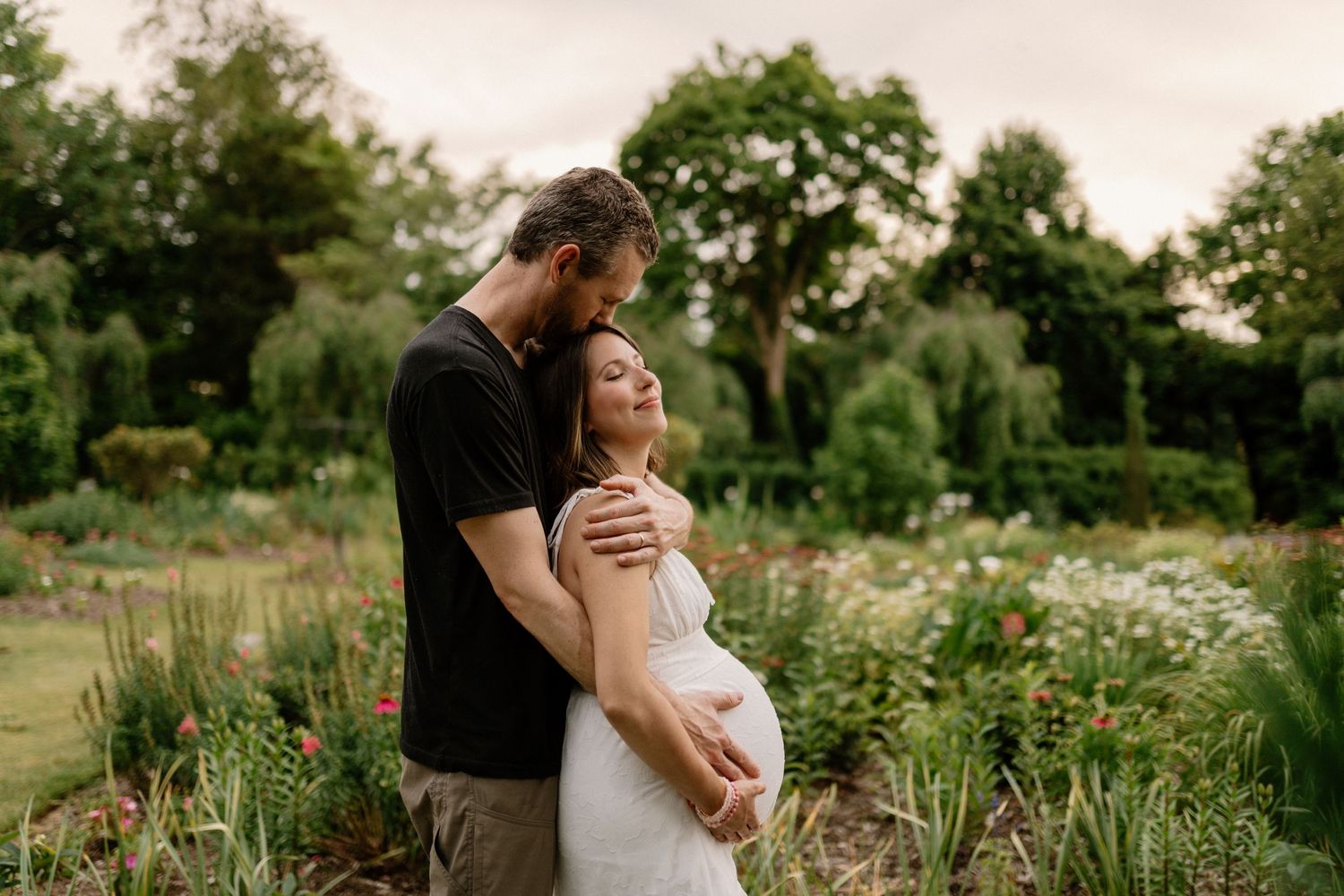A pregnant couple hug in a garden in North Carolina