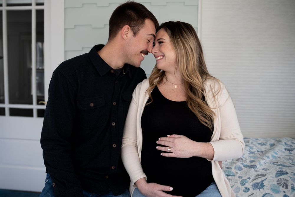 A couple shares an intimate moment while expecting a baby, dressed in black and cream colored clothing.